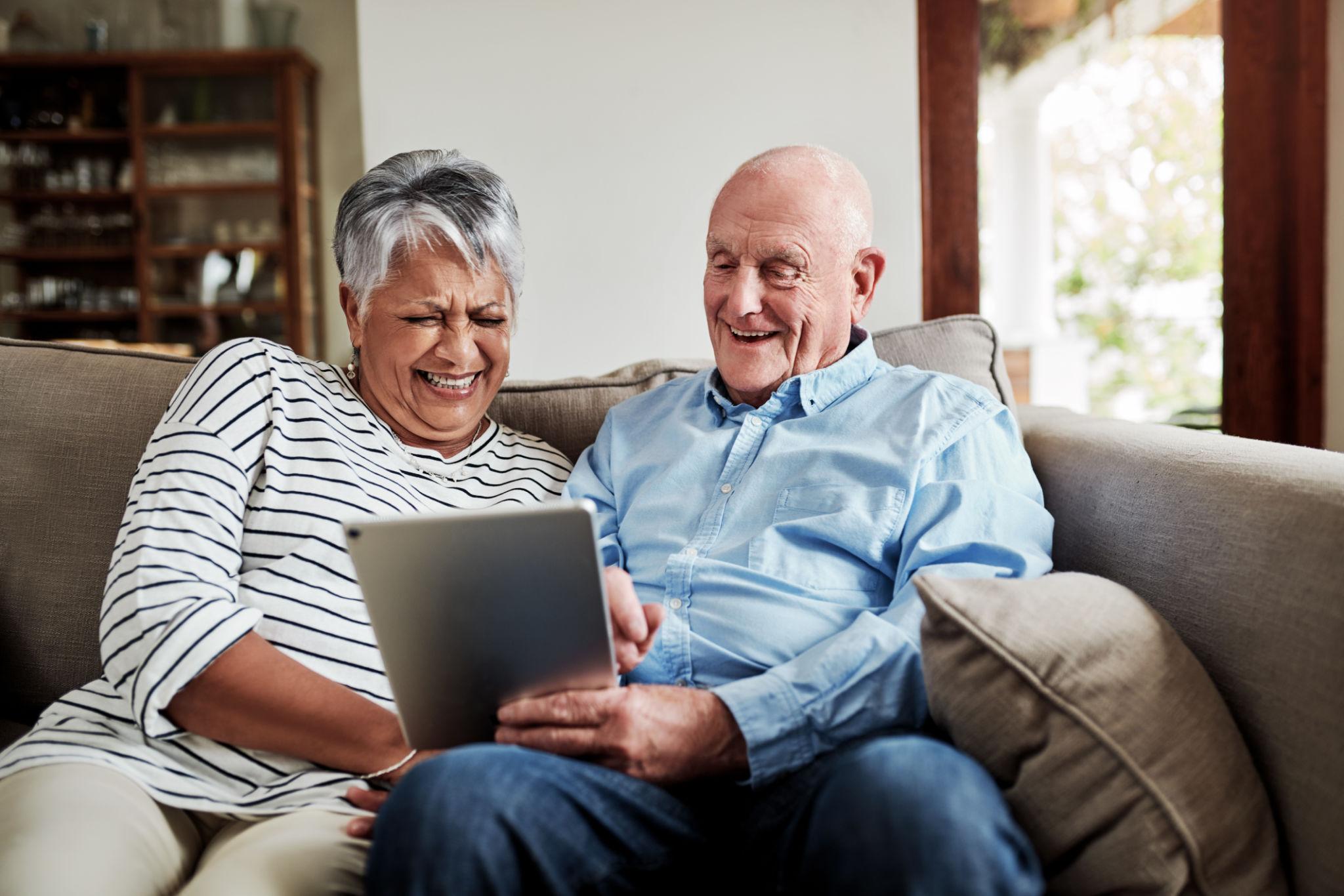 A smiling senior couple laughing together while using a tablet at home